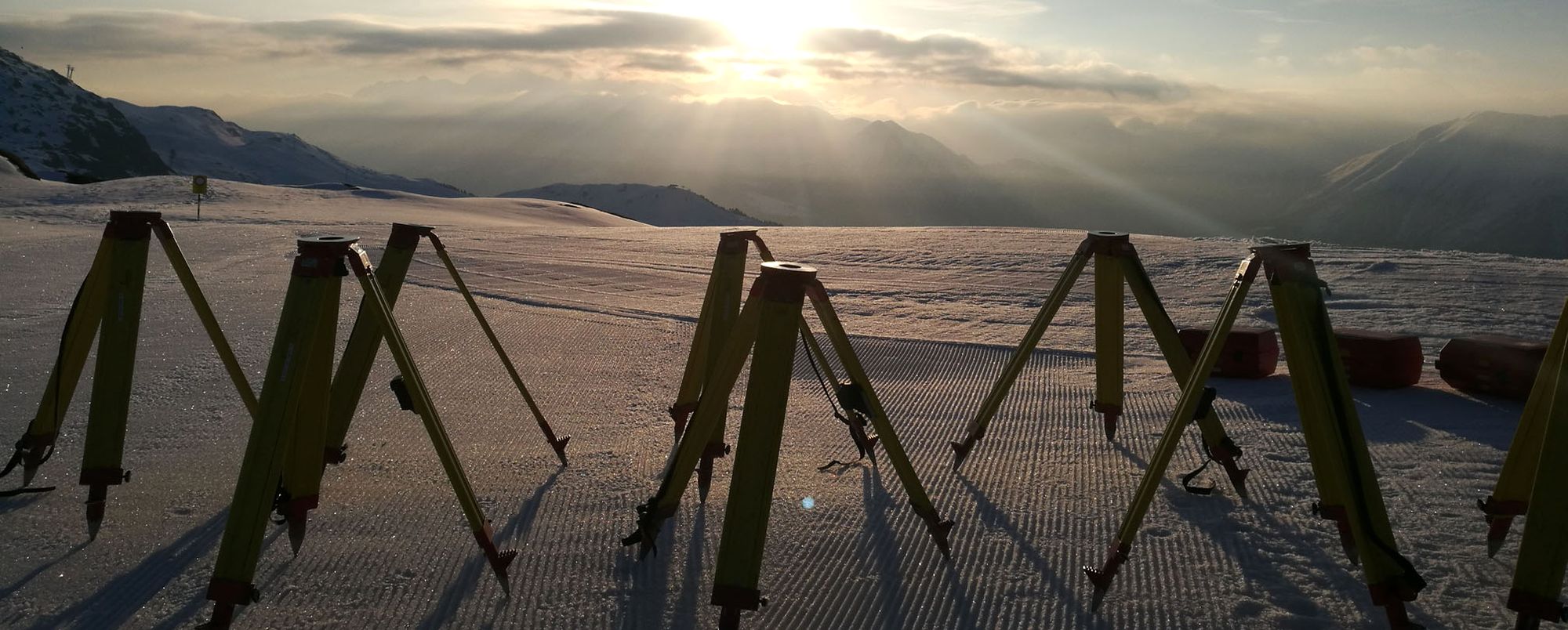 Vermessungsdreibeine im Schnee bei Abendlicht