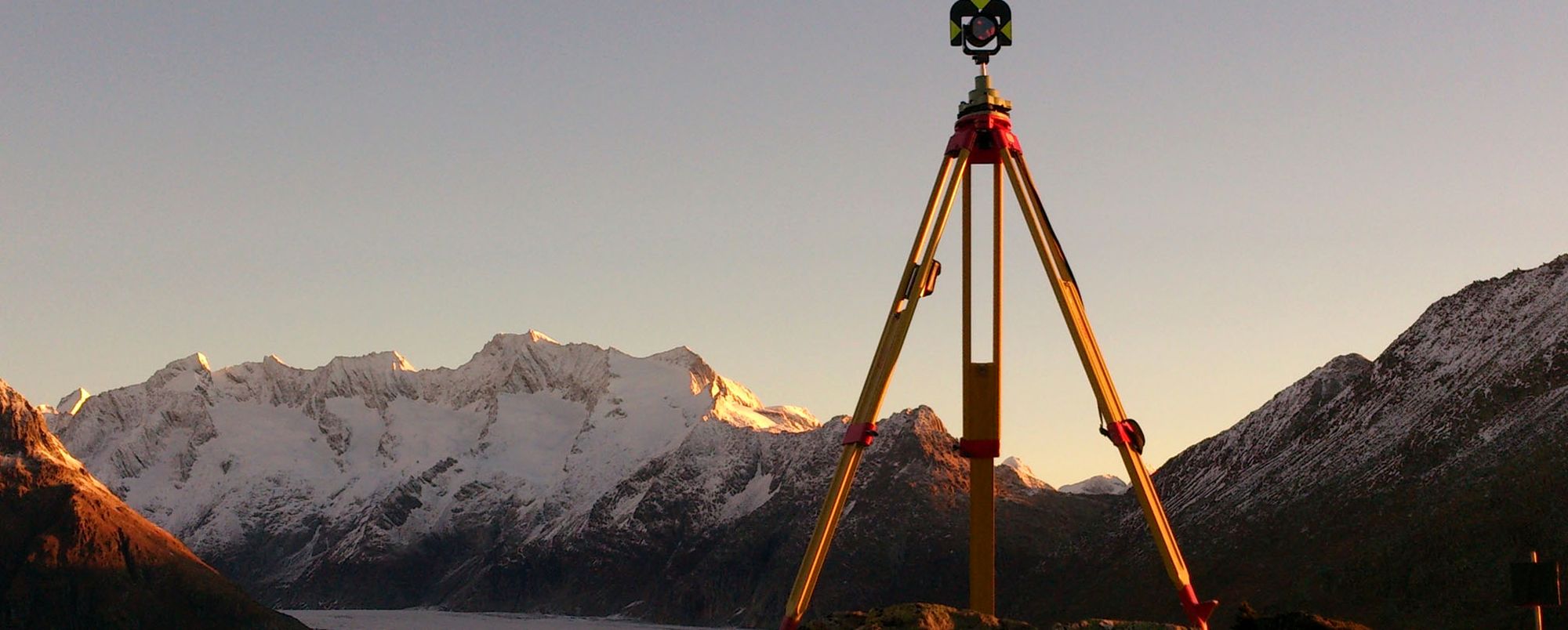 Vermessungsdreibein mit Reflektor vor den Walliser Alpen im Morgenlicht